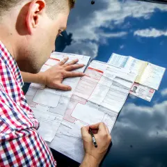 Mężczyzna w kratę wypełnia formularz oświadczenia o kolizji na masce samochodu.