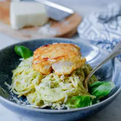 Pyszny makaron z rybą w panierce, posypany parmezanem i udekorowany bazylią. Danie wygląda apetycznie i zachęca do spróbowania.
