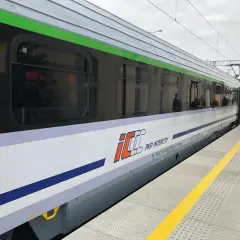 Nowoczesny pociąg EIC PKP Intercity stoi na peronie. Widać jego biało-fioletowy bok z zielonym pasem.