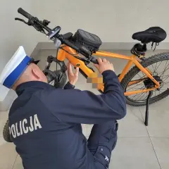 Policjant w czapce bada pomarańczowy rower elektryczny, próbując zrozumieć, jak działa rower elektryczny.