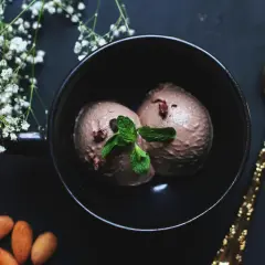 Deux boules de glace à la figue, garnies de menthe fraîche, dans un bol noir, avec des amandes et une cuillère dorée.