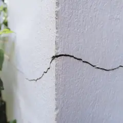 Pęknięcie na rogu białego budynku, które może świadczyć o tym, ile trwa osiadanie budynku. W tle zieleń roślin.