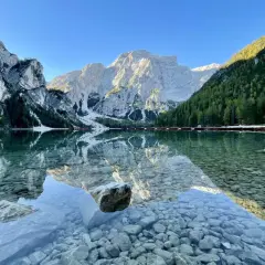 Der Pragser Wildsee spiegelt majestätische Berge und grüne Wälder. Kleine Boote liegen am Ufer.