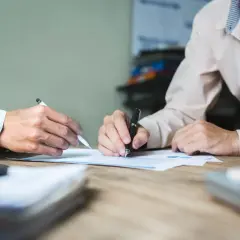 Dwie osoby przy biurku analizują dokumenty. Jedna z nich pisze, druga wskazuje coś na papierze. Może to być pomoc w procesie jak odzyskać pieniądze z obligacji Getin Noble Bank.