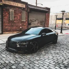 Czarny matowy samochód Audi na brukowanej ulicy przed ceglanym budynkiem.