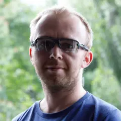 Mężczyzna w okularach sportowych na tle zieleni.