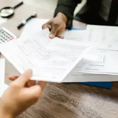 Dwie osoby analizują dokumenty, jak wypełnić in-1 przykład. Na stole kalkulator, lupa i długopis.