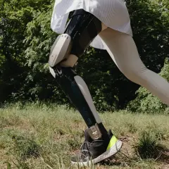 Eine Person mit einer C-Brace Orthese läuft durch grünes Gras.