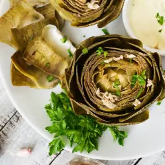 Deliciosas alcachofas al horno, tiernas y doradas, servidas con una cremosa salsa y perejil fresco. Un plato perfecto para disfrutar.