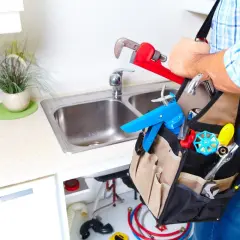 Hydraulik w fartuchu z narzędziami przy zlewie kuchennym.