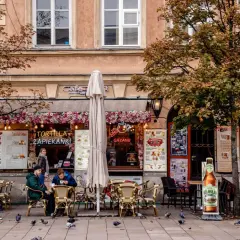 Jesienna Polska na weekend: kawiarnia z zapiekankami i grzanym winem, ludzie siedzą przy stolikach, gołębie spacerują po bruku.