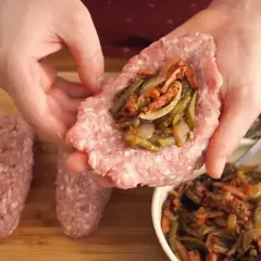 Ręce formują zrazy z mięsa mielonego, nadziewając je farszem z warzyw. Obok leżą gotowe zrazy.