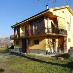 Casa gialla con balcone e vista collinare, un esempio di case economiche in campagna.