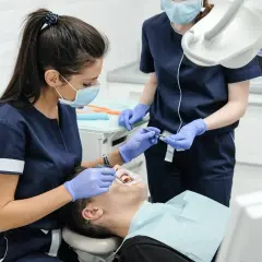 Dentystka w maseczce i rękawiczkach bada pacjenta. Czy u dentysty trzeba mieć maseczkę? Tak, dla bezpieczeństwa wszystkich.