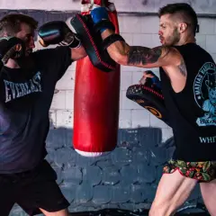 Two boxers train in a gym. One throws a punch while the other uses pads to parry boxing.