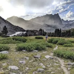 Wanderer auf dem Continental Divide Trail wandern durch eine bergige Landschaft mit einem See und bewaldeten Hängen.