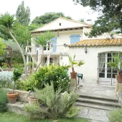 Maison en pierre avec jardin luxuriant, palmiers et lavande. Le panneau "Domaine des chênes truffiers" est visible.