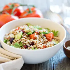 Salade de quinoa colorée avec tomates, concombre et canneberges dans un bol blanc.