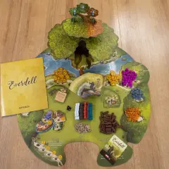 Na drewnianym tle leży plansza gry Everdell z instrukcją. Widać kolorowe zasoby, karty i pionki.