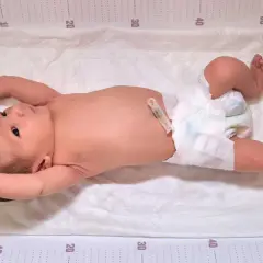 Neonato con pannolino e clip ombelicale, con le braccia sollevate, mostra i suoi riflessi neonatali su un telo con misurazioni.