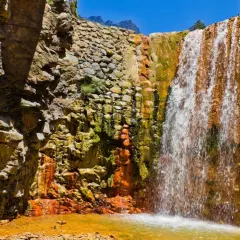 Ein Wasserfall stürzt über moosbewachsene, orangefarbene Felsen. Die Felsen sind von der Sonne beschienen, und das Wasser sammelt sich in einem goldenen Becken. Ein Stück Natur auf La Palma.