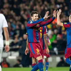 Piłkarze Barcelony, Piqué i Iniesta, świętują bramkę. Na pierwszym planie zawodnik w białej koszulce z numerem 3.
