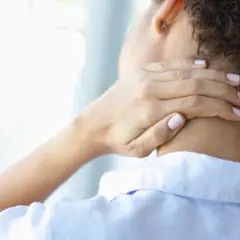 Frau mit steifem Nacken, die sich die schmerzende Stelle am Hals reibt. Was tun bei Nackenschmerzen?