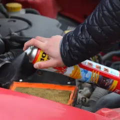 Ręka trzyma puszkę z preparatem do rozruchu silnika, rozpylając go w okolicy filtra powietrza. Czy odpalanie na plaka jest szkodliwe?