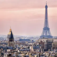 Eiffeltornet höjd över Paris takåsar i rosa skymningsljus. En gyllene kupol syns i bakgrunden.