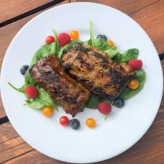 Grillowany udziec jagnięcy podany na liściach szpinaku z malinami, borówkami i pomidorkami koktajlowymi.