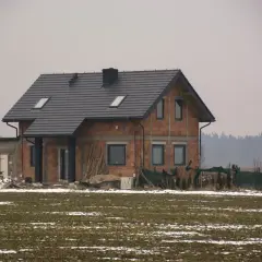 Dom w budowie, gdzie sprawdzić pozwolenie na budowę? Na placu budowy widać dom z cegły, dach i okna.