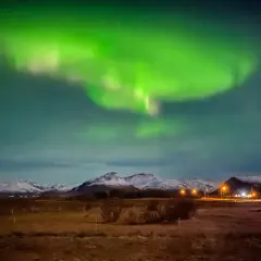 Zielona zorza polarna nad ośnieżonymi górami. Idealny czas, kiedy najlepiej lecieć na Islandię, by zobaczyć to zjawisko.