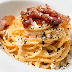 Spaghetti carbonara z chrupiącym guanciale, posypane parmezanem i czarnym pieprzem. To właśnie guanciale nadaje autentyczny smak.