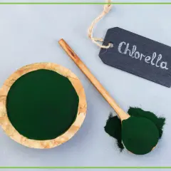 Chlorella tabletki na co pomaga? Zielony proszek w misce i na łyżce, obok tabliczka z napisem "Chlorella".