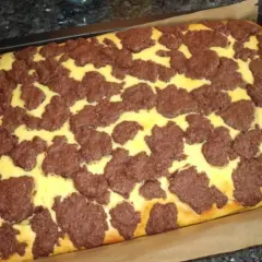 Ein frisch gebackener russischer Zupfkuchen im Blech, mit einem gelben Teig und dunklen Schokoladenstückchen darauf.