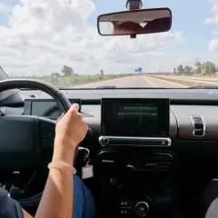 Vue du **rétro intérieur position nuit** d'une voiture. Mains sur le volant, route dégagée sous un ciel nuageux.