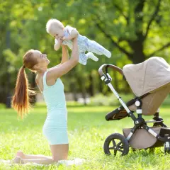 Mama podrzuca noworodka w wózku na trawie w parku.