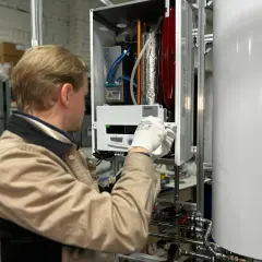 Technik w białych rękawiczkach sprawdza grzałkę miernikiem wewnątrz urządzenia.