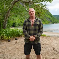 Alexander Strandberg Robinson står på en strand med gröna kullar och vatten i bakgrunden.