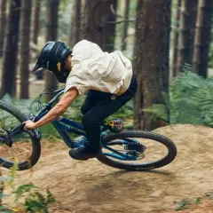 Rider in a forest, mid-air, demonstrating perfect mtb suspension tuning for a smooth landing.