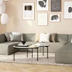 Gemütliches Wohnzimmer mit beiger Wand, einem großen grauen Sofa, Kissen und Kunstwerken.