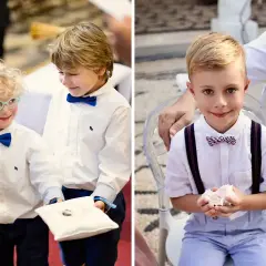 Uśmiechnięci chłopcy w eleganckich strojach, pełni powagi, niosące obrączki do ślubu. Jeden z nich ma okulary, drugi trzyma poduszkę z obrączkami.