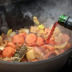 Verduras cocinándose en una olla, se vierte vino tinto. El vapor sube, indicando que el alcohol se evapora rápido.