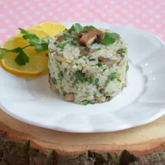 Aromatyczny ryż z pieczarkami, udekorowany natką pietruszki i plasterkami cytryny, podany na białym talerzu.