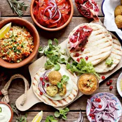 Vielfalt an arabischem Essen: Falafel, gefüllte Weinblätter, Bulgursalat, gegrilltes Gemüse, Hummus, Oliven und Granatapfel.