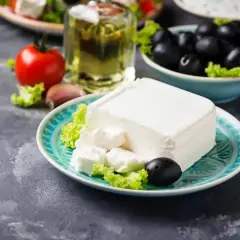 Un blocco di feta su un piatto turchese, con olive, pomodoro e olio d'oliva. La feta proprietà è l'ingrediente principale di questa deliziosa insalata greca.