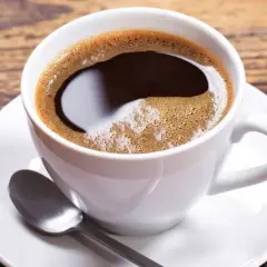 Aromatic coffee in a white cup, perfect for learning jak dobrze zaparzyć kawę sypaną. Na drewnianym blacie leży łyżeczka.
