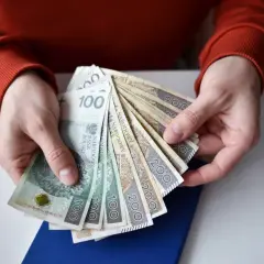 Dłonie trzymają plik polskich banknotów. Zastanawiasz się, ile wynosi składka zdrowotna dla emeryta?