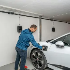 Mann lädt ein Elektroauto in der Garage. Die Installation ist für den Brandschutz ausgelegt.