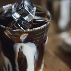 Ett glas iskaffe på snabbkaffe med mjölk som rinner ner längs glaset och isbitar som flyter i kaffet.